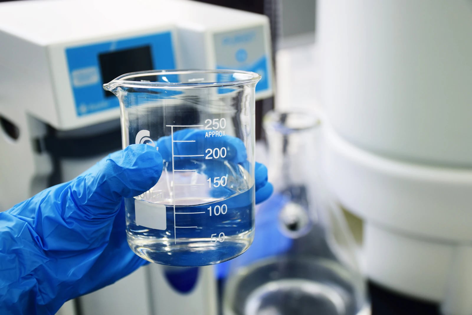 A gloved hand holding a beaker of purified water